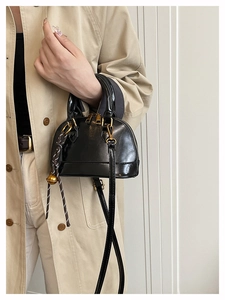 Detail of black patent leather shell bag featuring woven cord handle and gold bell charm