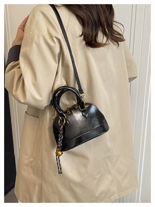 Close-up of black glossy shell bag with gold hardware worn as a crossbody with a beige coat