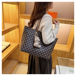 Detail of large dark checkered tote bag with brown handles and a plush bear pendant charm