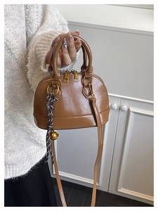 Detail of brown shell handbag with dual gold zippers and woven charm pendant accessory
