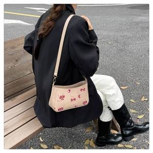 Detail of beige square crossbody bag with red cherry print and golden metal buckle