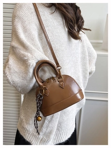 Brown mini shell handbag detail with woven bell pendant and adjustable shoulder strap