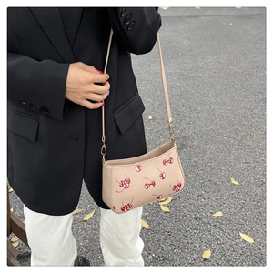 Close-up of beige shoulder bag with red cherry prints on a model with black suit
