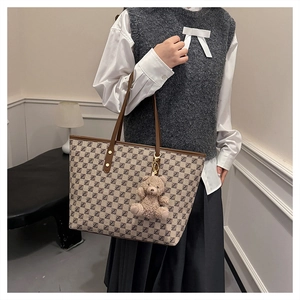 Detail of vintage tote bag featuring brown monogram pattern and plush bear charm decoration