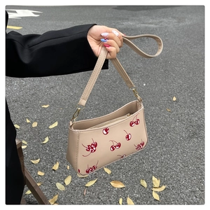 Detailed street style view of a beige handbag with red cherry print and metal zipper closure