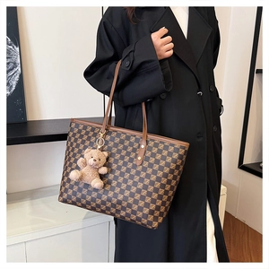 Detail of checkered tote bag with brown leather straps and cute plush bear accessory