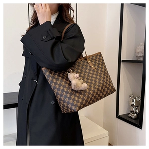 Detail of a large brown tote bag with pattern and cute plush bear charm on shoulder strap