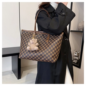 Detail of a large checkerboard tote bag with brown leather straps and a plush bear charm