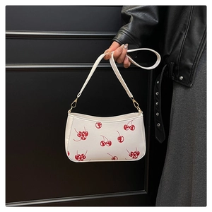 Close-up of white cherry print baguette bag with golden hardware on a shoulder strap