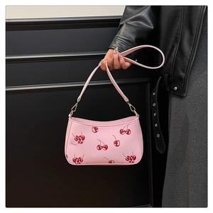 Detail of pink hobo bag with cherry print and golden hardware held by a model