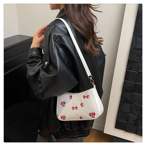 Detail of white leather shoulder bag with vibrant red cherry prints and golden metal hooks