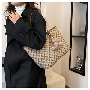 Detail of a patterned tote bag with brown leather trim and a plush bear pendant