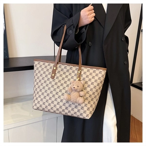 Detail of monogram tote bag with brown leather handles and cute plush bear charm