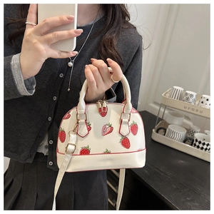 Detail of white shell handbag with red strawberry pattern and adjustable shoulder strap