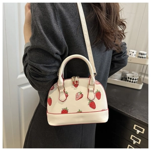 Détail du sac coquillage blanc à motif fraise porté par un mannequin en intérieur
