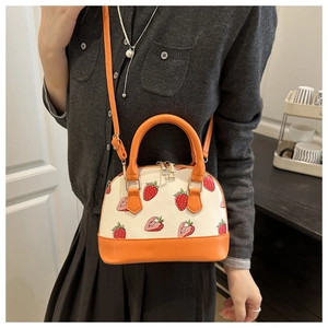 Détail d'un sac coquille orange avec imprimé fraises rouges et texture en cuir élégant