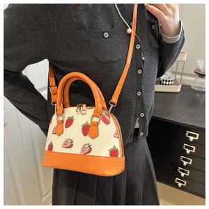 Detail view of mini strawberry shell bag in orange and cream with a long shoulder strap