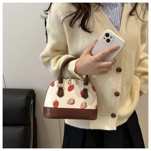Detail of strawberry print shell bag with brown leather base and dual gold zippers