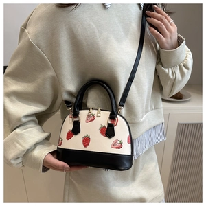 Detail of strawberry print shell bag with dual handles and adjustable black shoulder strap