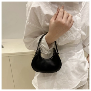 Detail of a black mini dumpling handbag with gold hardware held by a woman