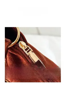 Detailed close-up of brown suede shoulder bag featuring a golden zipper and metal ring