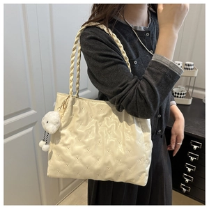Detail of cream tote bag with embossed bear pattern and braided handles on shoulder
