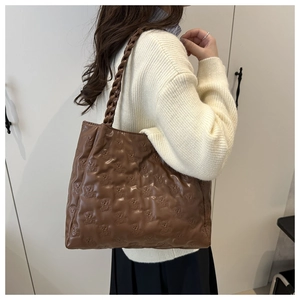 Brown tote bag with embossed bear pattern and braided strap shown on model shoulder