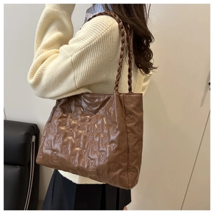 Detail of brown tote bag with embossed bear pattern and woven handles on shoulder