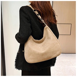 Detail of beige suede hobo bag featuring metal ring strap on model in tweed jacket