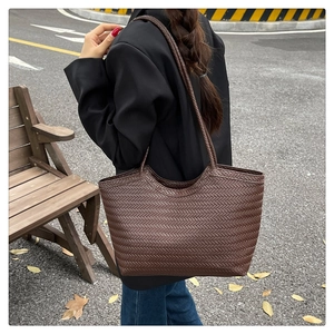 Detail of large brown woven tote bag showing the textured material and shoulder straps