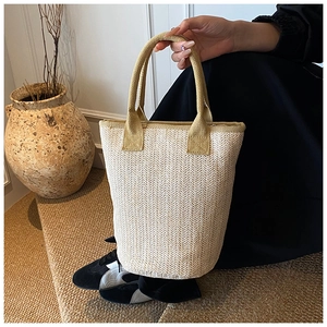 Detail of hand-woven straw bucket bag with herringbone pattern and neutral fabric handles