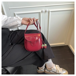 Macro detail of red faux leather saddle bag with cute strawberry charms and slim strap