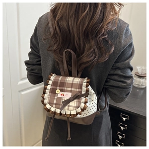 Detail of mini backpack featuring brown plaid flap, white ruffles and a cherry patch