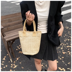 Detail of woven straw bucket bag with herringbone pattern and sturdy handles in outdoor setting