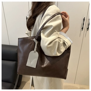 Detail view of large dark brown leather tote bag with stylish grey luggage tag decoration