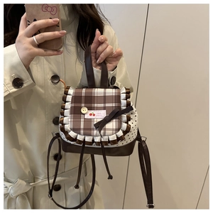 Detail of checkered mini backpack with lace trim and cherry embroidery held by a model