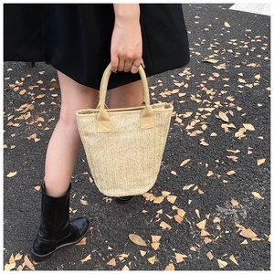 Outdoor shot of a woven straw bucket bag with round handles and a herringbone weave pattern