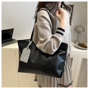 Detail of a large black soft leather tote bag with a decorative grey hangtag for work