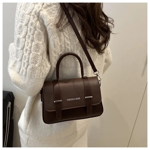 Détail du sac à main en cuir grainé marron foncé avec boucles argentées sur pull en maille