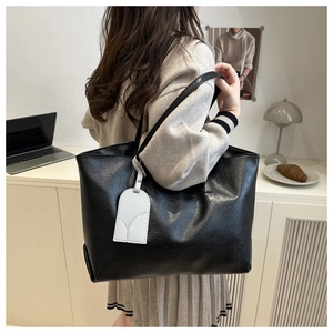 Detail view of a large black soft leather tote bag worn by a model in a workplace setting