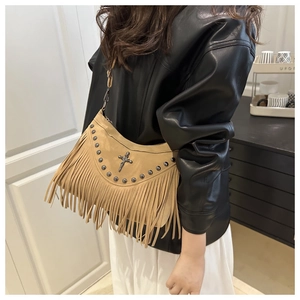 Detail of khaki suede half-moon bag featuring rivets, cross pendant, and long fringe