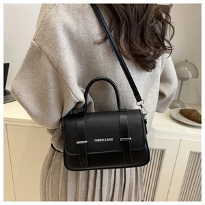 Modèle portant un sac bandoulière en cuir noir avec texture grainée et boucle métallique