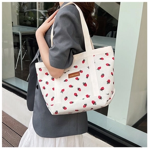 Detail of white corduroy tote bag featuring realistic strawberry prints and leather patch