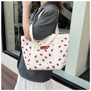 Corduroy tote bag with strawberry print and leather logo shown on a model's shoulder