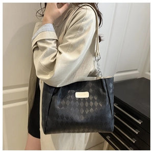 Detail of black quilted tote bag featuring silver chain strap and brand logo patch