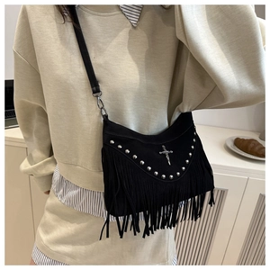 Detail of black suede crossbody bag featuring silver studs and long fringe with cross charm