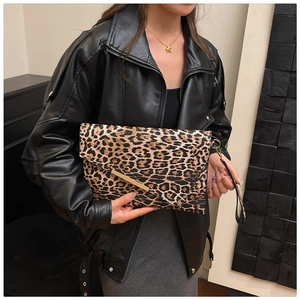 Détail d'une pochette léopard avec bordure métallique et dragonne portée par un mannequin