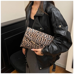 Chic leopard print envelope clutch bag with gold trim held against a leather jacket