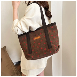 Detail of strawberry print corduroy tote bag with orange leather patch and zip closure