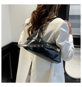 Detail of black glossy shoulder bag with metal grommet strap on a white blazer